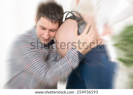 Happy future dad listening music with headphones to naked belly of his pregnant wife.