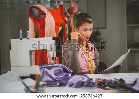 Vintage toned photo of a young woman designer sits in front of the sewing machine and looking at sketches of clothing.