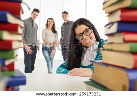 Portrait of a beautiful smiling girl with glasses sitting behind the many books in the foreground. Looking at camera.