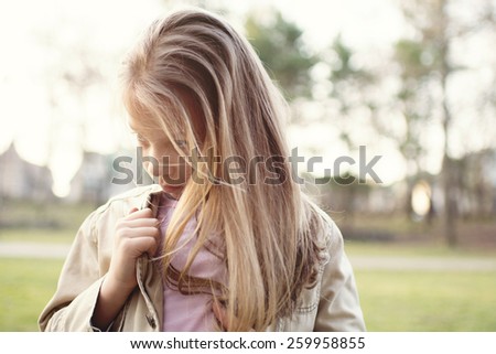 Close-up of a little girl standing alone outside with a sad expression on her face looking to the side.