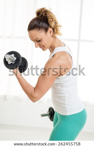 Beautiful young woman doing exercise to strengthen biceps with dumbbells at home.