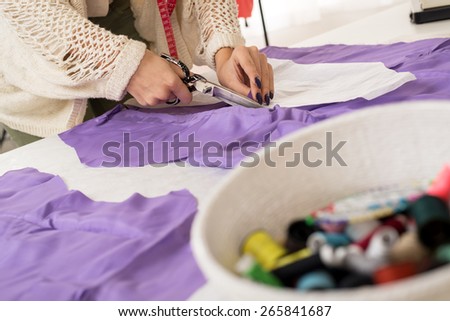 Woman hands cut with scissors material by sewing pattern.