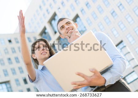 Young business couple with laptop, standing in front their company, look ahead at the height and thinking.