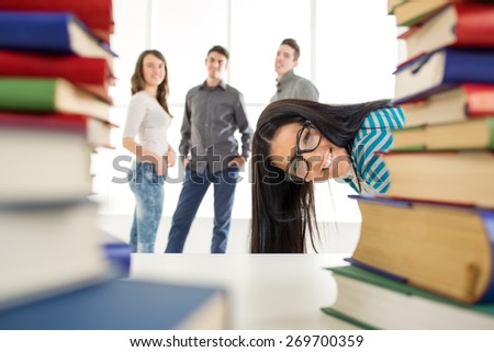 Portrait of a beautiful smiling girl with glasses stick out behind the many book\'s in the foreground. Looking at camera.