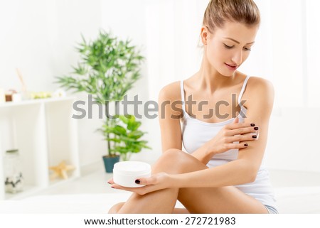 Beautiful young woman applying body lotion.