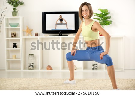 Young woman in sports clothes, doing exercises in the room, in front TV.