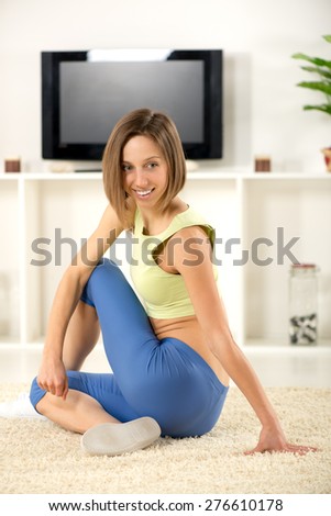 Young woman in sports clothes, doing stretching exercises in the room.