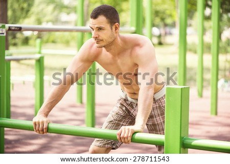 Naked muscle man resting after exercising in the outdoor gym.