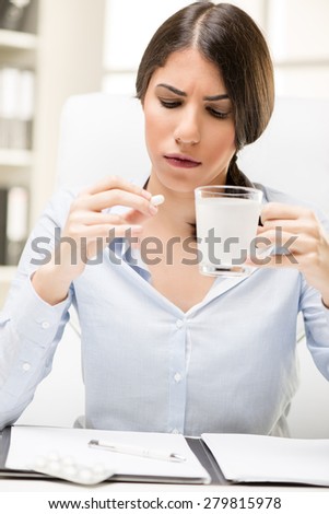Young beautiful woman takes a pill in the workplace, in the background you can see the shelves with binders.