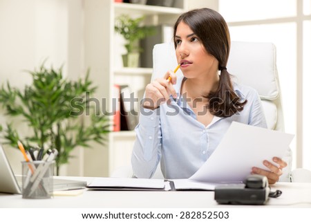 Portrait of a beautiful young businesswoman sitting in the office, biting pen and thinking.