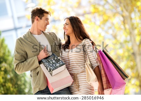 Close-up of a beautiful couple in love walking happily through town after shopping, hugging and carrying shopping bags in their hands.