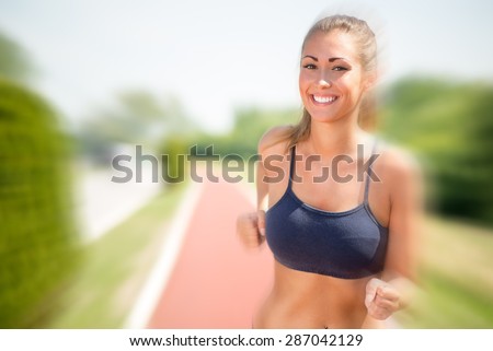 Happy young beautiful woman running on the tartan track. Looking at camera.