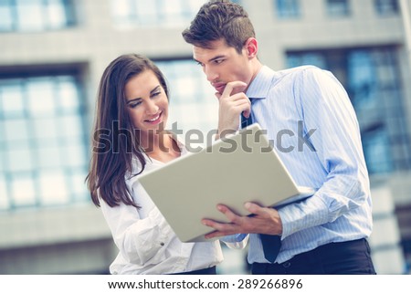 Close-up of a young business partners standing in front of office building and looking at laptop.