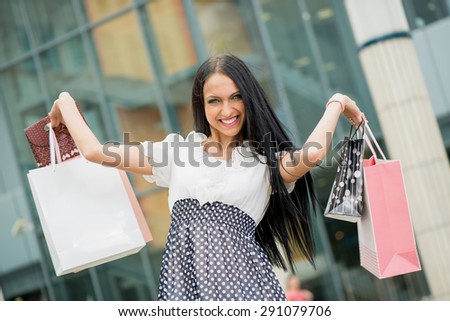 Portrait of a smiling young woman in shopping passes in front of window shopping mall carrying bags in their hands.