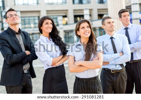 A small group of young business people standing in front of office building with arms crossed and with a smile on their faces looking in height.