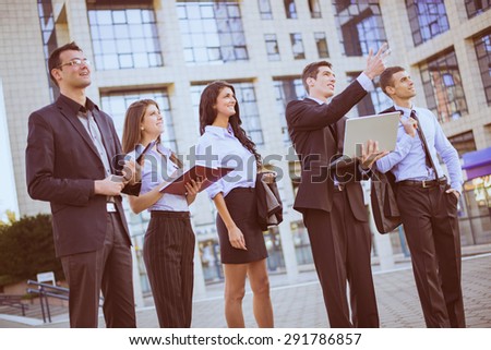 Young businessman with laptop in front of office building outstretched fingers of the hand, aimed at heights, explaining his colleagues business plan.