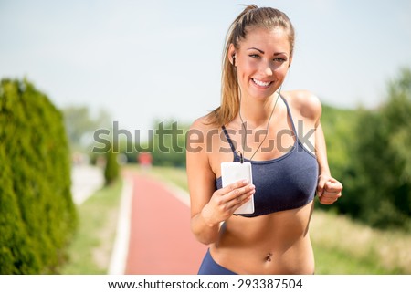Smiling girl running on the tartan track and listening music on headphones. Looking at camera.