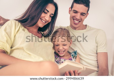 Beautiful Happy young mother and father and their cute daughter sitting at home and reading book