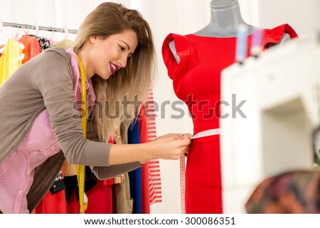 Young beautiful girl with a tape measure, takes measure of clothing which standing on a mannequin.