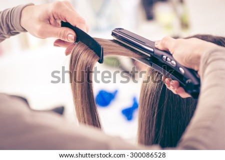 Close-up of a hairdresser straightening long brown hair with hair irons.