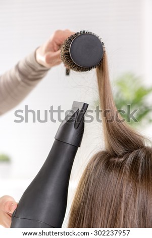 Close-up of a drying brown hair with hair dryer and round brush.