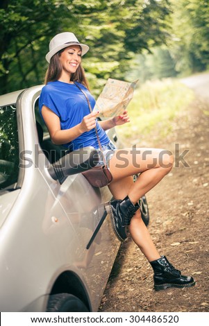 Young beautiful woman standing leaning at car in the forest and looking a map.