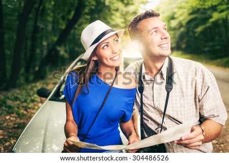Young travelers standing before a car in the forest, holding map and looking at destination.