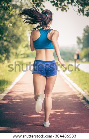 Happy young beautiful woman running on the tartan track.  Rear view.