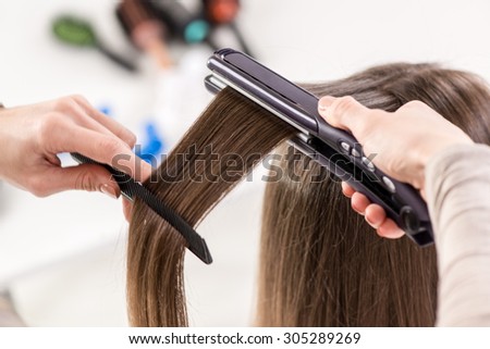 Close-up of a hairdresser straightening long brown hair with hair irons.