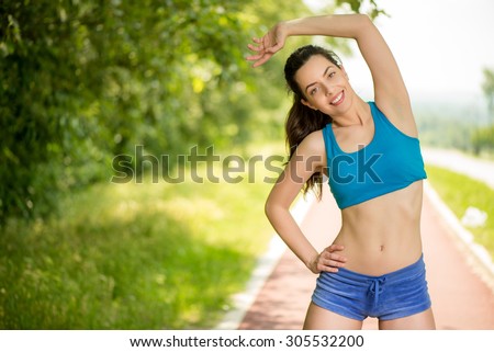 Happy young beautiful woman doing exercise on the tartan track.