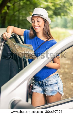 Young beautiful woman standing leaning at car in the forest and looking a map.