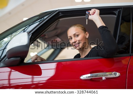 Young beautiful happy woman showing the keys of new car through car window. Looking at camera.
