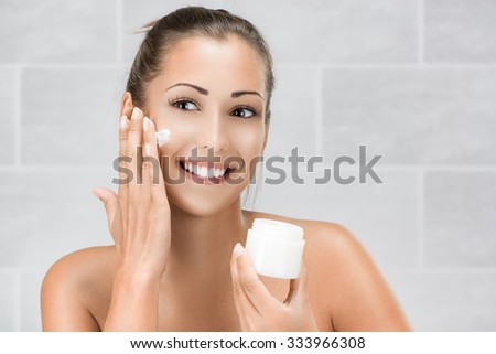 Cute girl preparing to start her day. She is applying moisturizer cream on face.