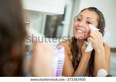 Beautiful smiling young woman removing make up with a facial wipe in front of mirror.