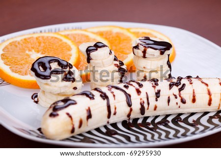 Fresh fruit dessert with banana and orange topped with melted chocolate on white plate