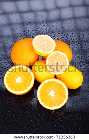 Juicy delicious oranges and lemons on reflective table with water drops
