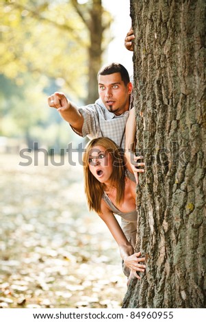 Young couple behind tree looking something scary