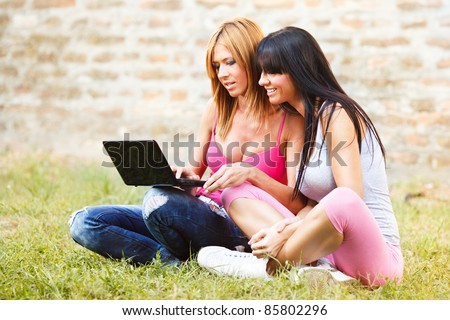 Happy young girls with laptop browsing the internet, and chat with friends, outdoor