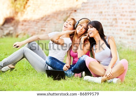 Three young beautiful girls listen music from notebook, outdoor