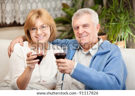 Happy senior couple toasting their anniversary with red wine at home ambient