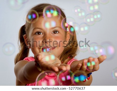 Pretty young girl enjoys catching bubbles that are floating in the air