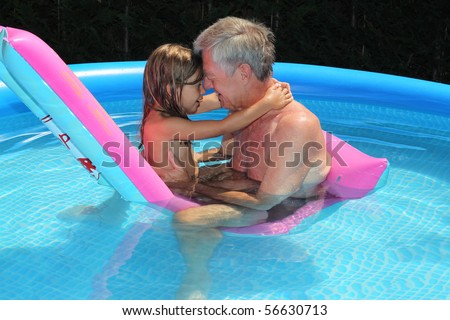Grandfather and granddaughter cuddling on a lilo in a swimming pool