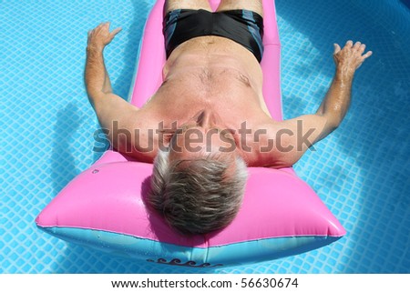 Older man floating on a pink lilo and sunbathing in a swimming pool