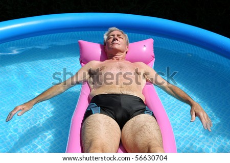 Older man floating on a pink lilo and sunbathing in a swimming pool