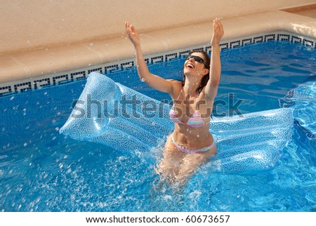 Woman sitting on a lilo in a swimming pool and splashing water above her head