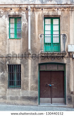 A weathered facade with a window, a balcony, a grilled window and a metallic door. The picture has been taken in the SarriÃ?Â  quarter of Barcelona, where old buildings and traditional facades abound.