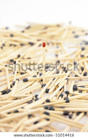 One unused match (red head) stands up among dozens of used matches (grey and burned) that lay around.