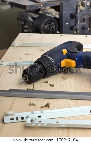 Furniture parts and electric screwdriver on a wooden table in workshop