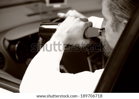 Drunk man in car with a bottle beer in sepia photo