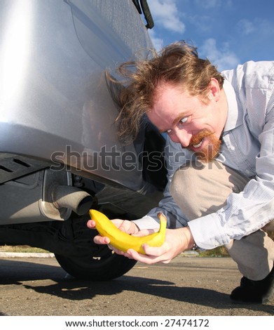 Man putting banana into car exhaust pipe - stock photo